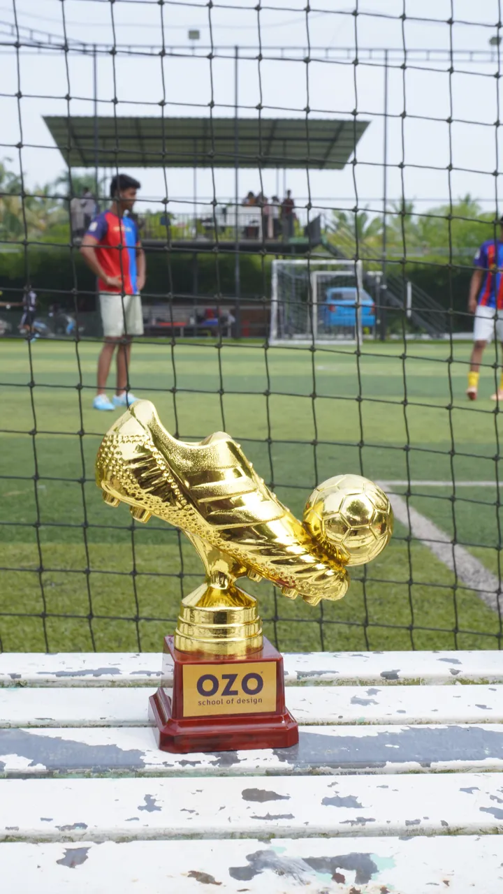 A golden boot trophy with the OZO logo beside the football turf